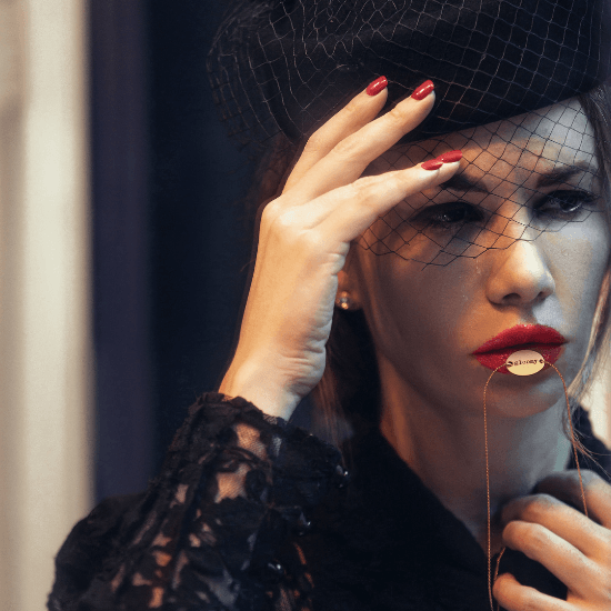 Woman in vintage funeral attire presses necklace to mouth